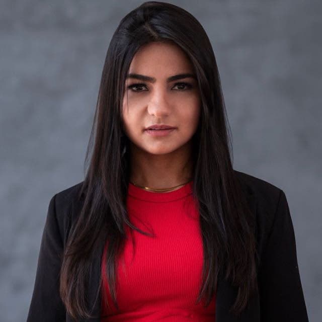 Portrait of a woman with long dark hair wearing a red shirt against a gray background.